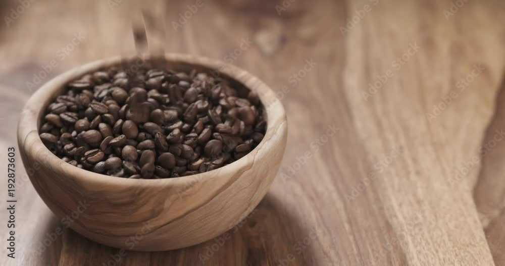 Slow motion coffee beans falling into wood bowl on table Slow motion coffee beans falling into wood bowl on table