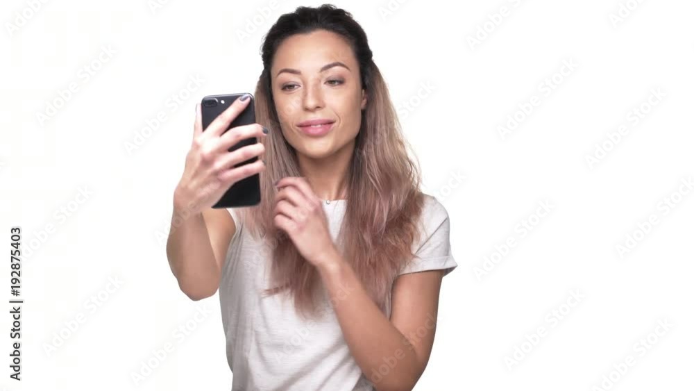 Portrait of gorgeous young woman making selfie on her smartphone, isolated over white background closeup. Concept of emotions Portrait of gorgeous young woman making selfie on her smartphone, isolated over white background closeup. Concept of emotions