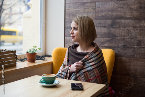 Woman drinking coffee in the morning at cafe. Soft focus on the eyes. Sellphone on table.