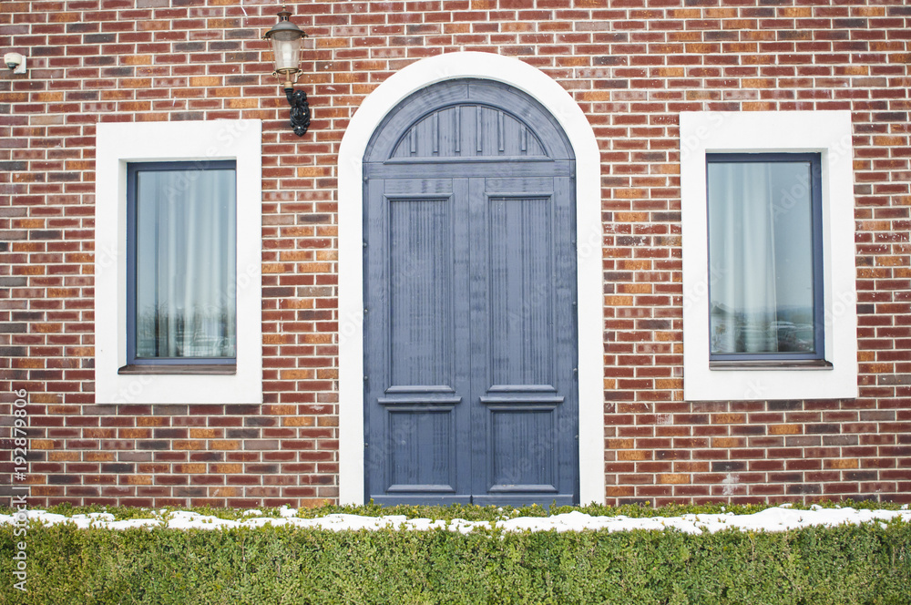 The facade of the house with a blue arched door and square windows on the sides The facade of the house with a blue arched door and square windows on the sides