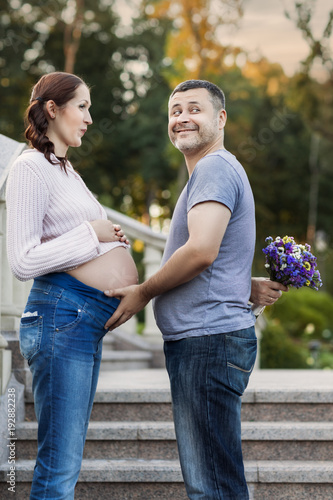 Portrait of a married couple. Husband holds his pregnant wife by the belly