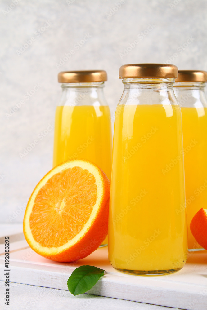 Glass bottles with fresh orange juice with orange slices and yellow tubes on a light gray table. Glass bottles with fresh orange juice with orange slices and yellow tubes on a light gray table.