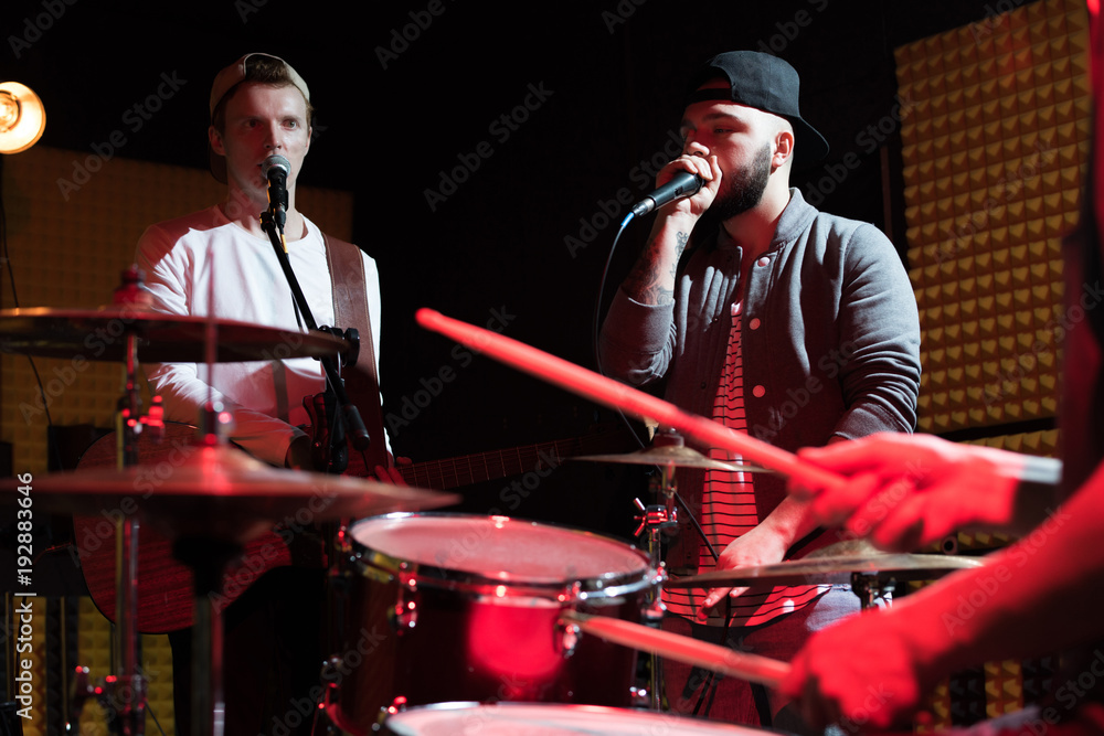 Portrait of hip-hop singer performing with his band in recording studio, drum set in foreground, scene lit by red light Portrait of hip-hop singer performing with his band in recording studio, drum set in foreground, scene lit by red light