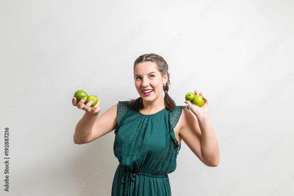 Fototapeta premium Young woman stands in front of white background with hands full of fruits