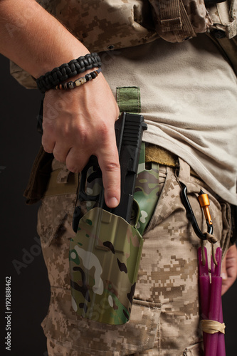 Close-up of a gun that properly holds a man in a military desert uniform and body armor on a black background in the Studio. The man grabs a gun out of the holster for self-defense