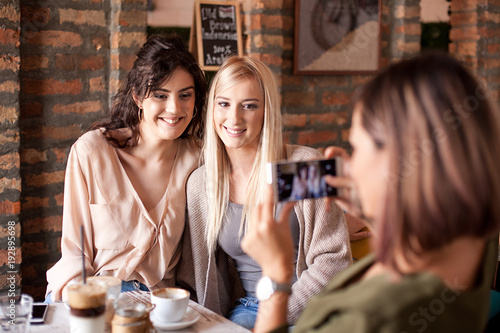 Girl friends in cafe taking a photo with smart phone. Three women drinking coffee together and having fun. 