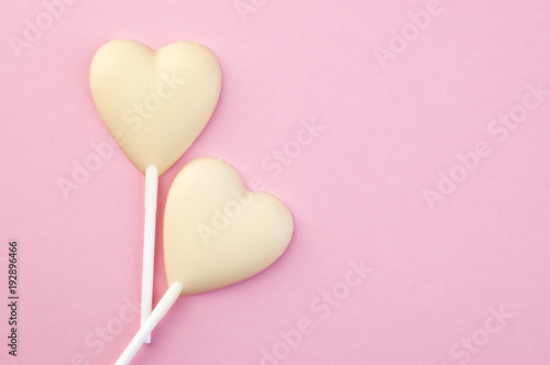 Two white chocolate candy hearts on pink