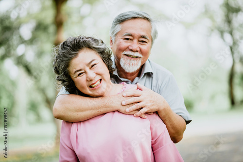 Happy smile senior Asian couple enjoying quality time at the park. A man embracing woman closely. success marriage life.