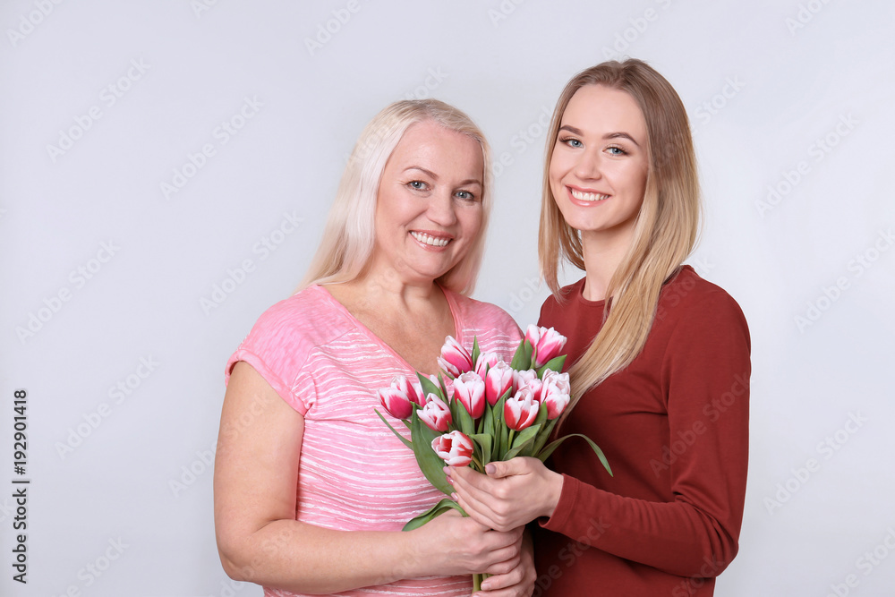 Young daughter and mother with bouquet of flowers on light background