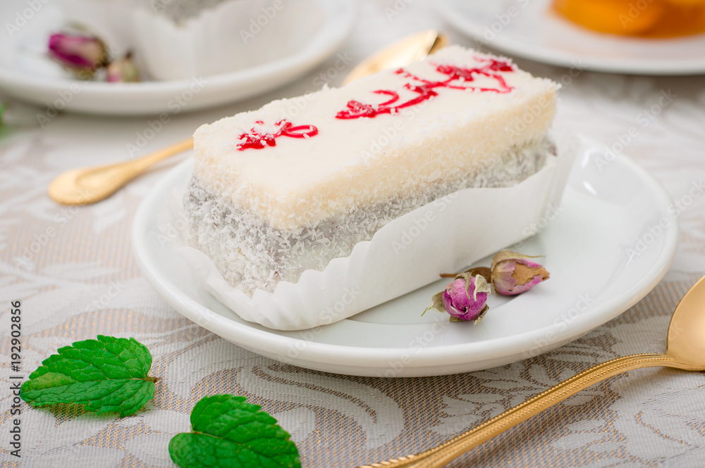 A fresh piece of coconut cream cake on a white plate with a whipped cream and peach jelly. White background. Top view A fresh piece of coconut cream cake on a white plate with a whipped cream and peach jelly. White background. Top view
