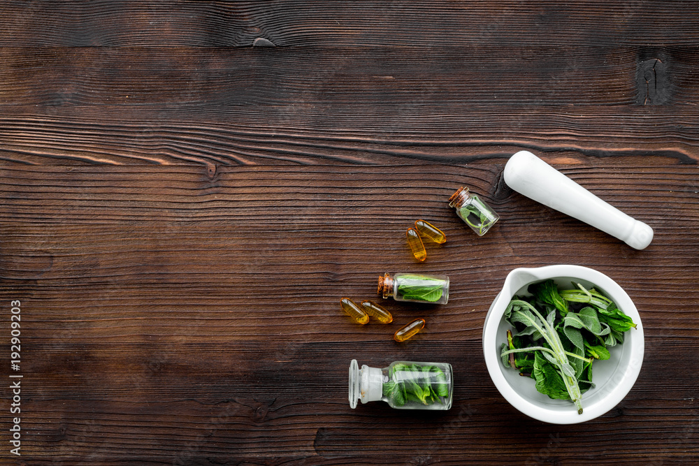 Harvest medicinal herbs. Greens in mortar bowl and herbs in small bottles on dark wooden background top view copy space Harvest medicinal herbs. Greens in mortar bowl and herbs in small bottles on dark wooden background top view copy space