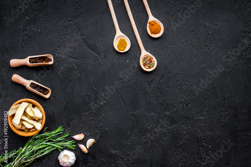 Condiments, seasoning and spices concept. Dry spices in wooden spoons on black background top view copy space