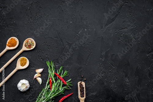 Condiments, seasoning and spices concept. Dry spices in wooden spoons near ginger, rosemary, chili pepper on black background top view copy space