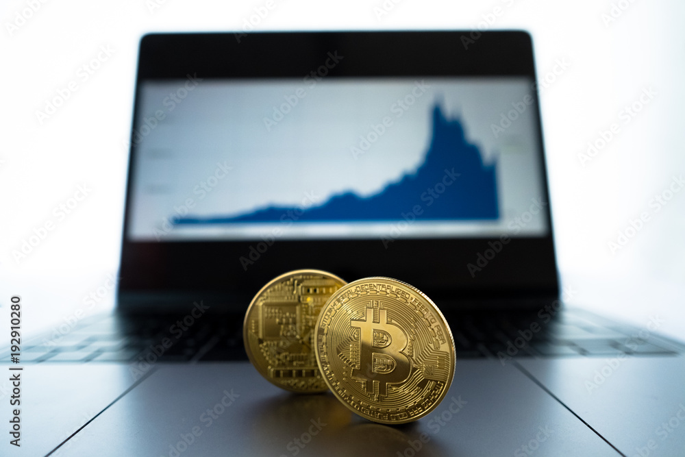Physical Bitcoin in front of laptop showing area chart of market performance