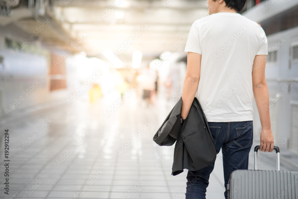 Young Asian casual man holding suit and luggage while walking in airport terminal