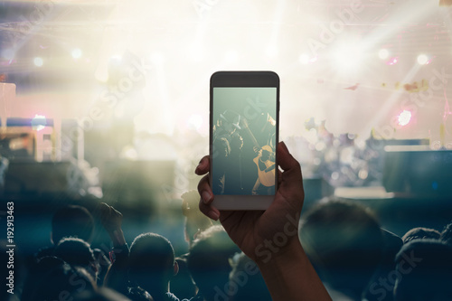 Female hand holding mobile smart phone taking video record or Live stream of Concert crowd with super star songer and silhouettes of Music fanclub with show hand action, musical and concert concept