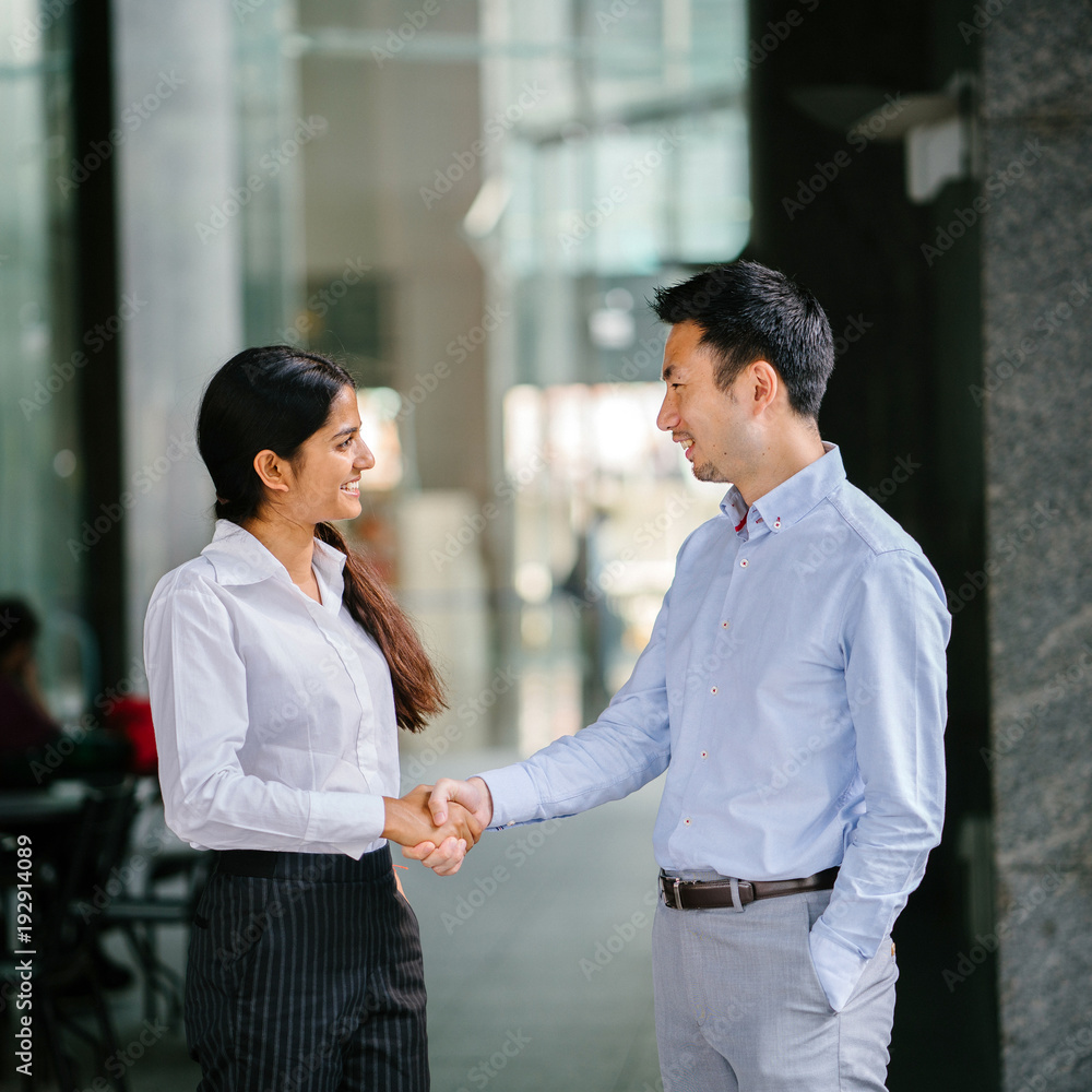 An image of two team mates or colleagues shaking hands for success while standing in their office during day. They are smiling in a relaxed way and both wearing a professional outfit. An image of two team mates or colleagues shaking hands for success while standing in their office during day. They are smiling in a relaxed way and both wearing a professional outfit.