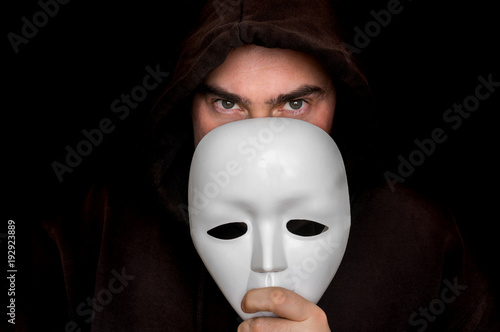 Foto Mysterious man in black hiding his face behind white mask
