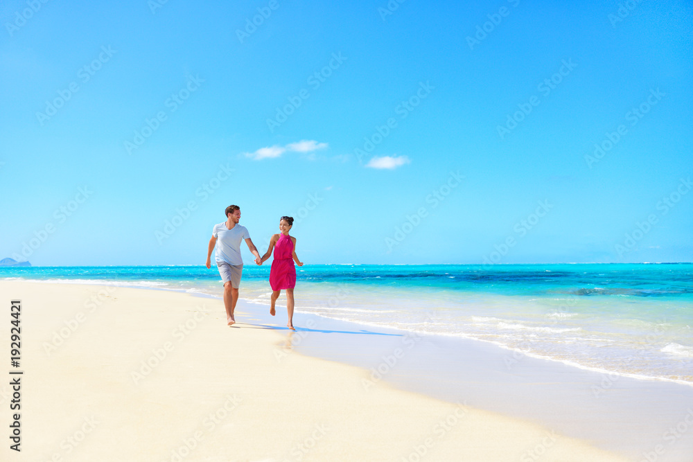Beach honeymoon couple holding hands walking on white sand beach. Newlyweds happy in love relaxing on summer holidays on Caribbean beach. Travel vacation concept.