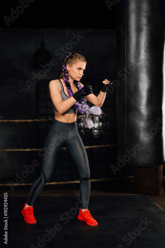 Young woman trains in boxing ring with heavy punching bag.