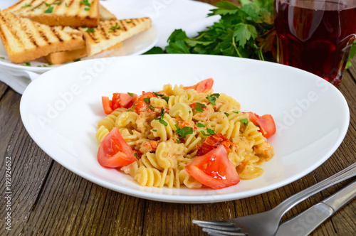 Warm salad with seafood in a white bowl on a wooden background. Pasta Radiatori with crayfish, shrimp, tomatoes, herbs and creamy garlic sauce.
