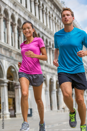 Running runner couple man and asian woman tourists jogging in Venice. Summer sport athletes training on travel vacation sightseeing on Piazza San Marco Square, Venice, Italy, Europe.