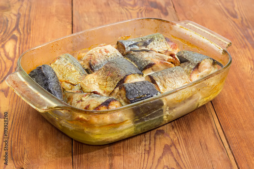 Baked mackerel in glass casserole pan on old table closeup photo