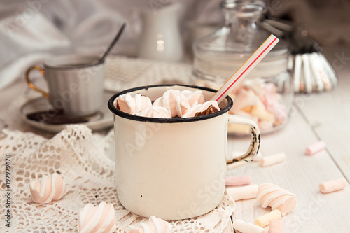 Mug of hot chocolate drink with marshmallow candies on top and chocolate chips on white background.