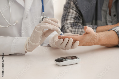 Doctor measuring blood sugar level of diabetic patient in clinic, closeup