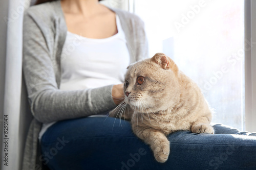 Young woman with cute pet cat sitting on windowsill at home