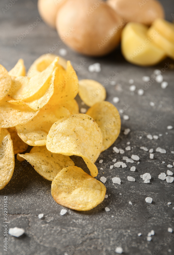 Yummy crispy potato chips with salt on grey table