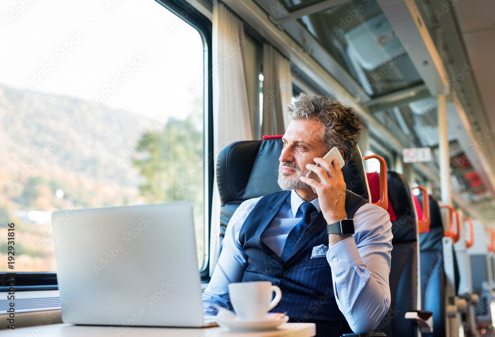 Mature businessman with smartphone travelling by train. - obrazy, fototapety, plakaty 