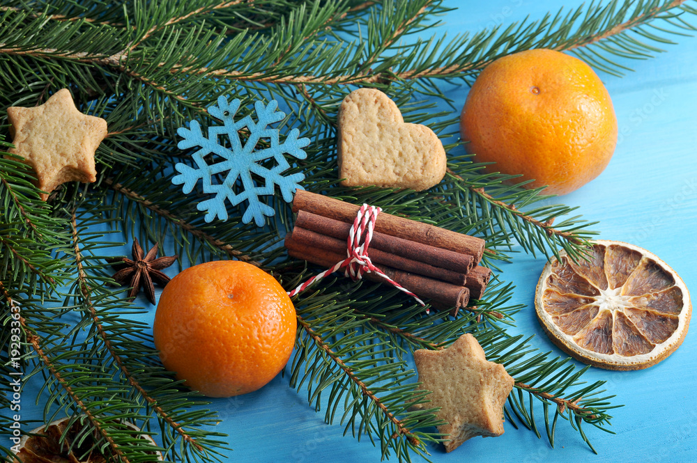 Christmas composition of spruce branches, mandarin, cookies, cinnamon sticks, dried orange slices and a Christmas tree toy in the form of snowflakes. Blue wood background. Close-up. Macro photography.