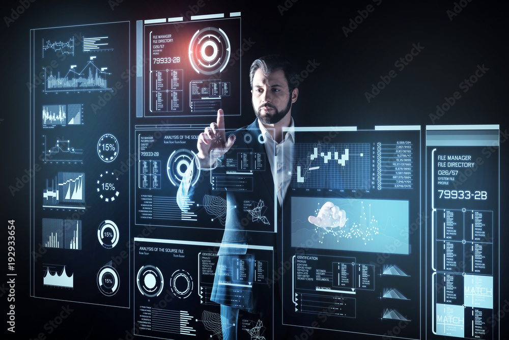 Obraz premium Careful programmer. Attentive experienced smart programmer looking elegant in his suit while standing in front of a futuristic device and touching the screen of it
