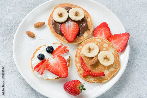 Funny colorful breakfast pancakes with animal faces for kids on white plate. Top view