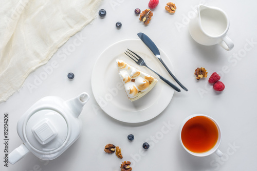 top view of piece of cake with berries and tea on white table