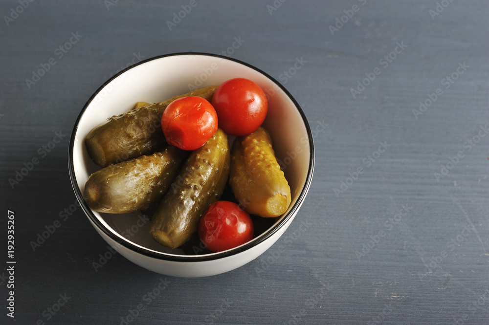 Marinated cucumbers and cherry tomatoes in a white deep dish. Dark wooden background. View from above. Close-up. Marinated cucumbers and cherry tomatoes in a white deep dish. Dark wooden background. View from above. Close-up.