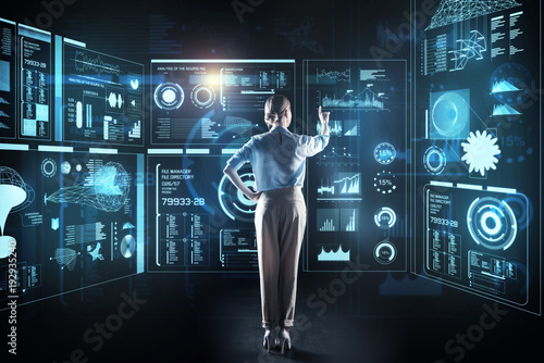 Fototapeta Naklejka Na Ścianę i Meble -  Elegant programmer. Calm clever reliable programmer standing in front of a giant transparent device while thinking about the new information and touching a futuristic screen
