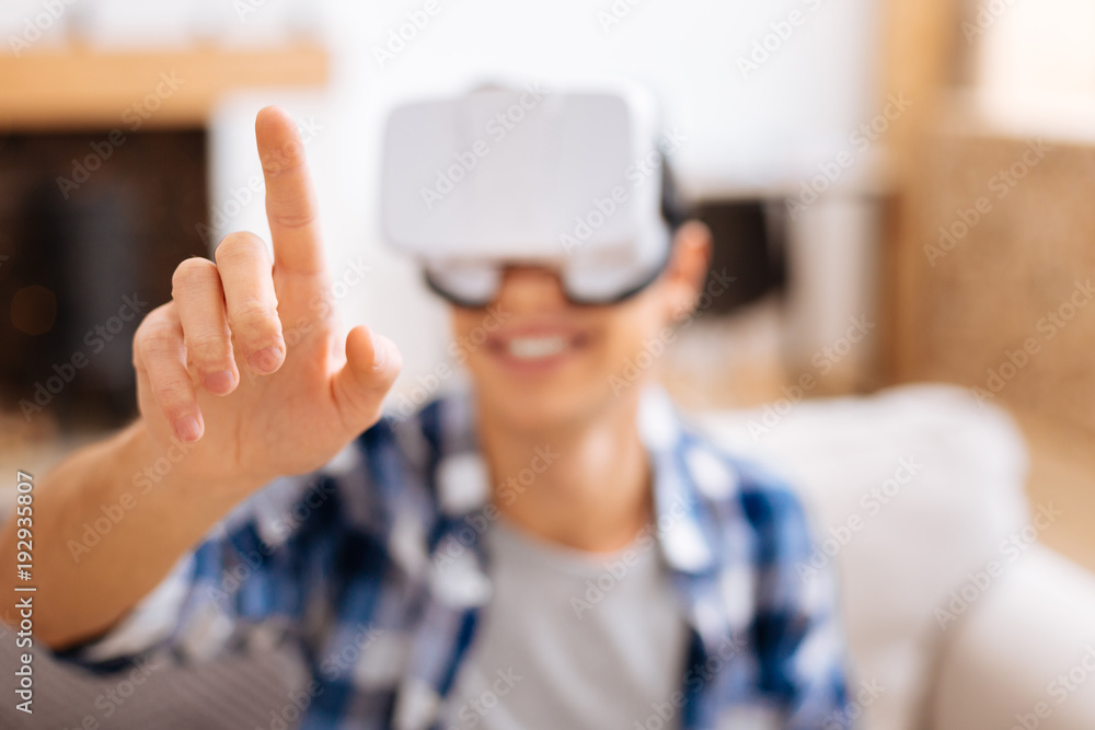 Entertaining. Alert stylish adolescent smiling wearing a VR headset and relaxing while sitting on the sofa and touching the imaginary picture