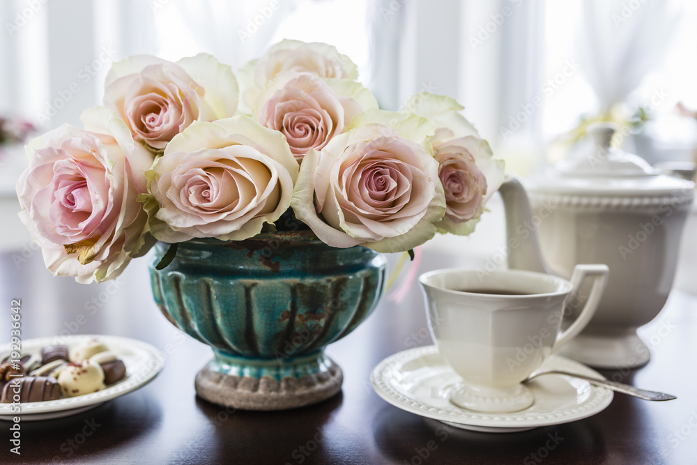 Cup of tea and bouquet of beautiful roses in an vintage vase on the table. Cup of tea and bouquet of beautiful roses in an vintage vase on the table.