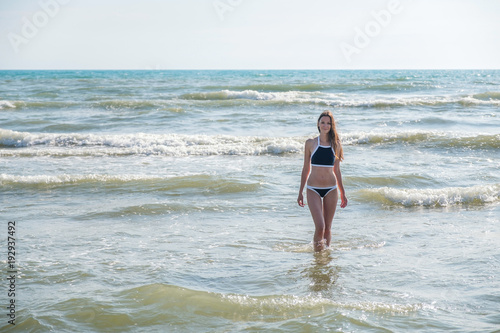 Woman bruenette with long hair in blue bikini going to swim in the wave's sea. Front view. Close-up