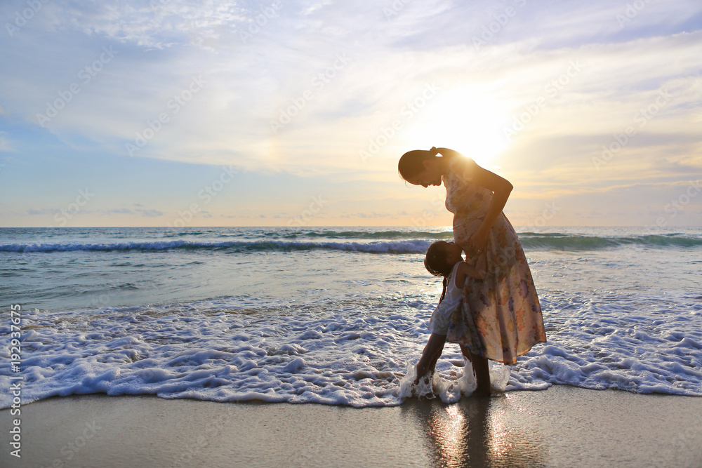 Fototapeta premium Silhouette pregnant mother embracing daughter relaxing on the beach at sunset.