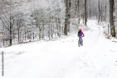 Young woman cycling in the forest in wintertime on a snowy road