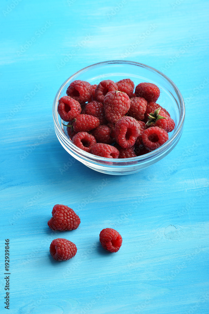 Berries of ripe raspberries in a glass cup. Close-up. Blue wood background. Berries of ripe raspberries in a glass cup. Close-up. Blue wood background.