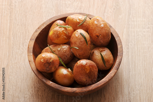 Potatoes in a wooden bowl. Prepared in a peel with sea salt, garlic and rosemary. Light wooden background. Closeup.