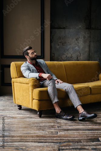 handsome stylish elegant man sitting on couch in loft interior