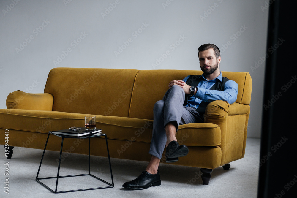 fashionable man sitting on yellow sofa with alcohol drink on table near fashionable man sitting on yellow sofa with alcohol drink on table near