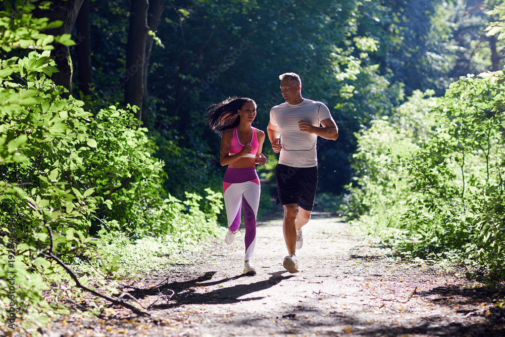 A man and a sportive woman Jogging in the woods and talking.