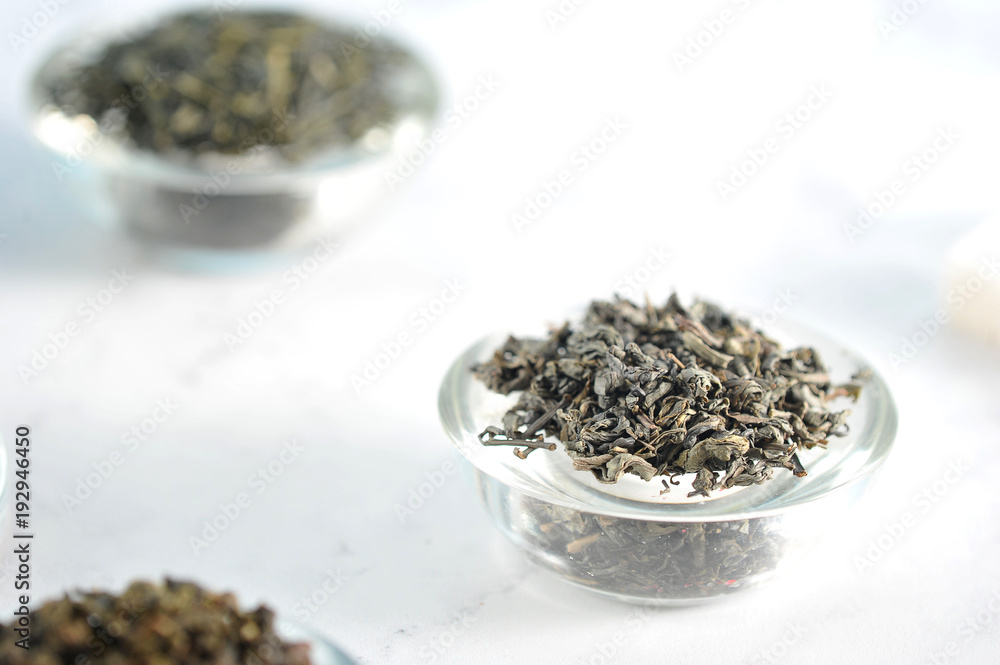 Black tea and green tea in separate glass saucers. Light background. Close-up. Macro photography. Black tea and green tea in separate glass saucers. Light background. Close-up. Macro photography.