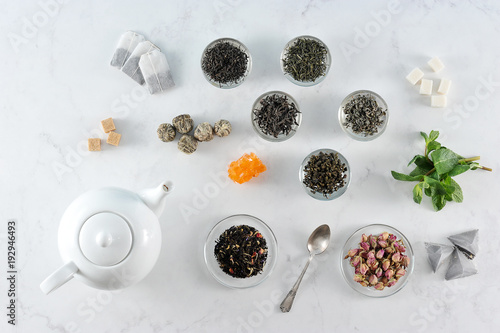 Assorted tea and teapot. In the frame black large leaf tea, green, green with jasmine, milky oolong, flavored tea, tea in balls. Mint leaves, dried flower buds, sugar, tea bags. View from above. 
